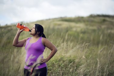 Female jogger drinking diet supplements like Plexus from bottle