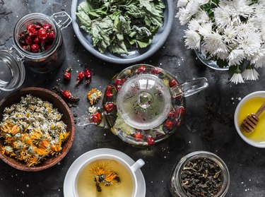 Herbal tea with currant, mint, raspberry leaves, chamomile and calendula flowers, rose hips, teapot on a dark background, top view. Flat lay