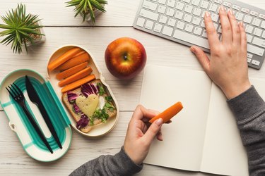 Woman eating healthy dinner from lunch box at her working table
