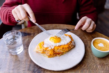 Man eating Croque Madame sandwich with cheese and fried egg