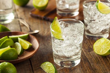 A glass of clear tequila on the rocks with lime on a wooden table