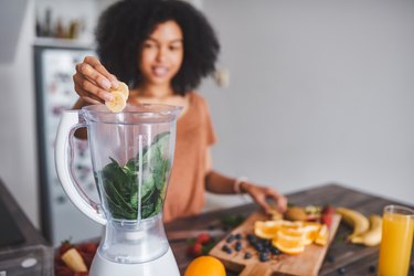 女子将水果和菠菜放入搅拌机中制作冰沙