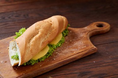 Fresh and tasty sandwich with cheese and vegetables on cutting board over wooden background, selective focus.