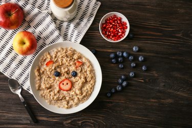 Plate with creative porridge for children on dark wooden table