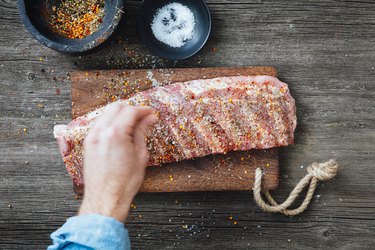 Hand seasoning ribs with spices on wooden counter