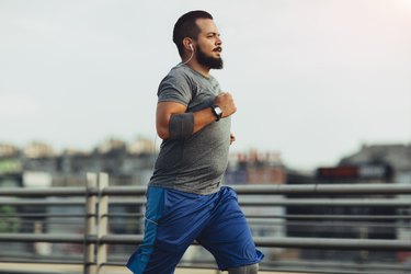 a bearded adult wearing a gray short-sleeve shirt and blue shorts running a marathon outside