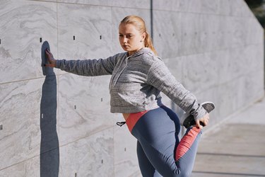 Woman doing a quad stretch while bracing herself against a wall outside