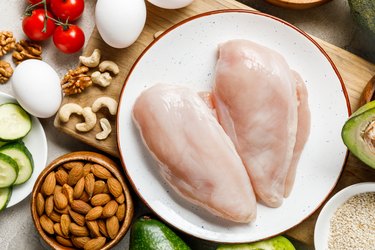 top view of fresh raw chicken breasts near nuts, eggs and vegetables, ketogenic diet menu