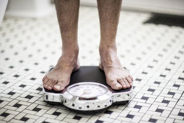 An adult man standing on an analog scale in a black-and-white bathroom