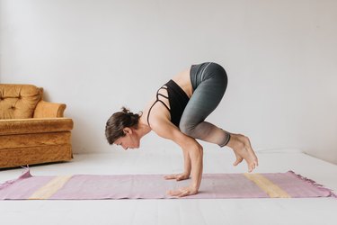 Woman doing crow pose while practicing yoga in studio