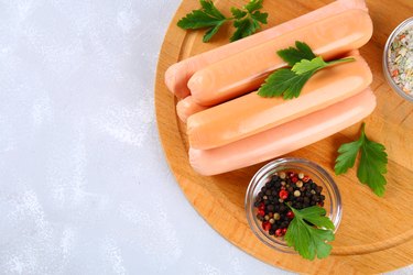 Sausages on a wooden board on a gray concrete table.