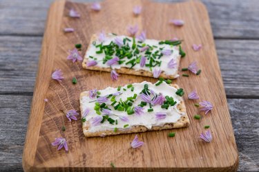 Two dairy and lactose-free vegan cream cheese spread made from cashew and macadamia nuts on crackers with fresh chopped chives and edible chive flowers on a chopping board with shallow depth of field