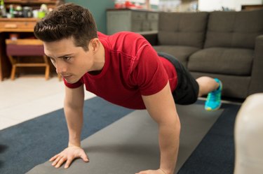 adult wearing a red t-shirt and black shorts doing push-ups for bigger shoulders at home