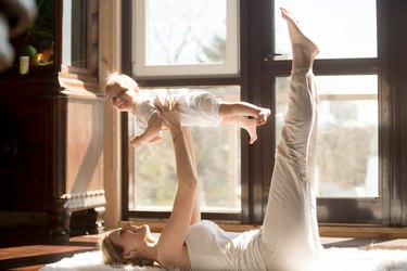 Young yogi mother exercising at home, holding her baby daughter
