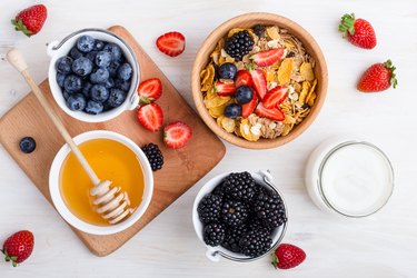 Healthy breakfast with cereal, fresh berries, yogurt and honey over white rustic wooden table viewed from above