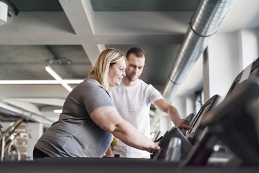 Attractive overweight woman with her personal trainer running on treadmill in modern gym.