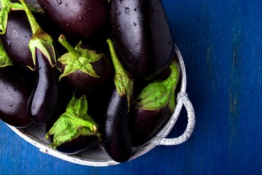 Fresh eggplant in grey basket on blue wooden table.Rustic background. Top view. Copy space. Vegan vegetable.