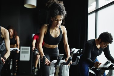 Woman riding out of saddle during indoor cycling class in fitness studio