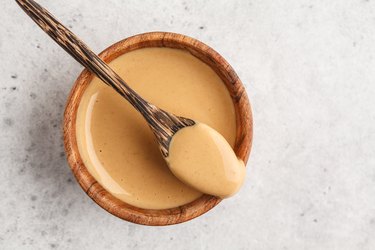 Creamy homemade peanut butter in wooden bowl, top view.