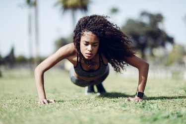 Sporty young woman doing push-ups on lawn