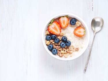 Oatmeal porridge with strawberry, blueberry, granola on white wooden background. Healthy breakfast. Top view, copy space