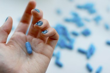 Woman is holding blue pill in her hand.