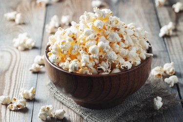 A wooden bowl of salted popcorn on a wooden tabled