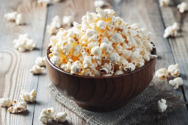 A wooden bowl of salted fiber in popcorn at the old wooden table. Dark background. selective focus