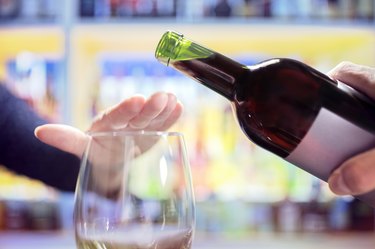 Person rejecting more alcohol from wine bottle in bar