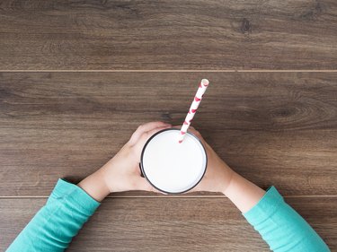 Child holding a glass of milk on dark rustic table