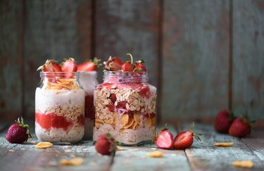 Tasty healthy breakfast. Overnight raw oatmeal in jars with organic strawberries on turquoise background