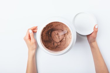 View from above female's hands opened chocolate protein powdercontainer