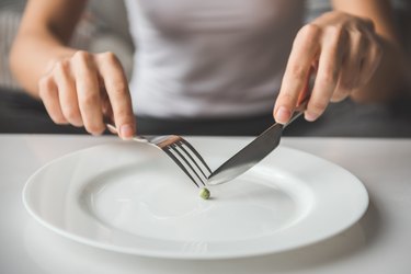 A woman cutting a pea with a knife and fork; diet concept