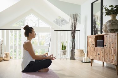 Woman sitting in Lotus pose in her living room doing a beginner yoga routine