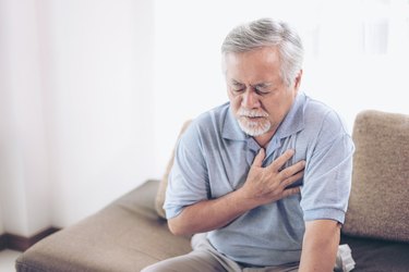 A senior Asian male holding his chest and suffering from stabbing pain when breathing