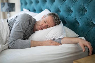 An older man sleeping on bed in bedroom
