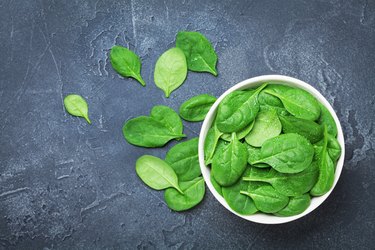 Green spinach leaves in bowl on black table top view. Organic and diet food.