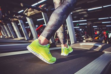 Theme of sport and weight loss. Close-up of the foot of a young strong woman in a light green sneakers on a simulator, running in the gym. Preheating before training, cardio training