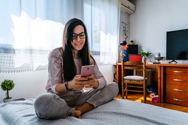 Smiling woman using phone in bed