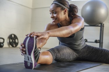 Smiling athlete stretching legs on exercise mat in health club