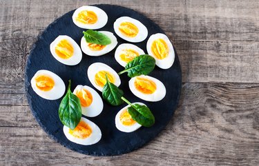 Fresh green spinach baby leaves and boiled eggs cut in a half on wooden background