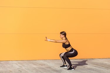 Young attractive woman practicing fitness, doing bodyweight squat exercise, yoga chair pose, working out, wearing black sportswear black pants and top,