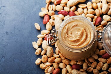 Peanut butter jar and heap of nuts on vintage table with copy space for text.