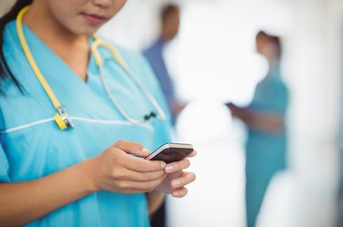 Mid section of nurse text messaging on mobile phone
