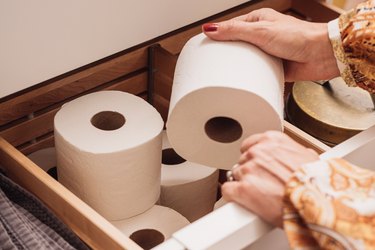 A woman reaching for a roll of toilet paper stored in a bathroom drawer