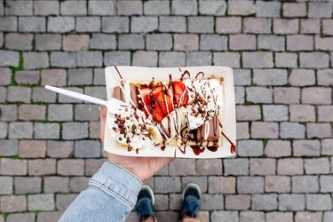 Eating Belgian waffle with sweet toppings and fresh fruits at the town square, personal perspective view