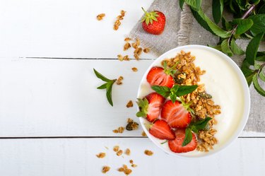 A bowl of dietary fitness breakfast: yogurt, granola, fresh strawberry, mint on a white wooden background. Proper nutrition. Top view.