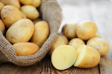 A bag of raw potatoes with one potato cut in half.