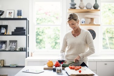 an adult wearing a v-neck cream sweater pre-slicing vegetables in the kitchen to promote healthier eating
