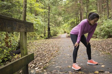 Tired woman resting hands knees after run woods